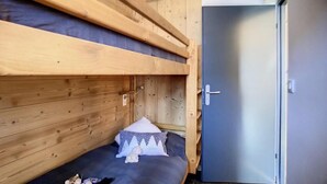 Una cama individual en literas con cabecera de madera, una mesita de noche pequeña y un almohadón.