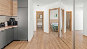A modern kitchen with a built-in microwave, a coffee machine, and a refrigerator. There is a wooden floor and a glass partition leading to a bedroom with a bed and a bathroom with a sink. - Villa Marko by Aneo Travel (Ledenice)