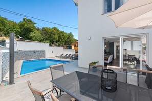 A modern outdoor pool area with a dining table and chairs, a covered patio, and a view of the surrounding neighborhood. - Villa Marko by Aneo Travel (Ledenice)