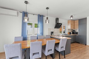 Une cuisine moderne avec des meubles gris, une table à manger en bois et des luminaires suspendus.