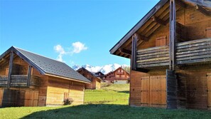 A row of wooden cabins with sloped roofs, set against a backdrop of snow-capped mountains. - Chalet, view mountain, swimming pool, terrace, parking, tv, ski locker, 55m², La Joue du Loup (Agnières-en-Dévoluy)
