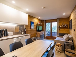 Uma cozinha compacta com eletrodomésticos modernos, uma área de refeições com mesa de madeira e um espaço de estar aconchegante com sofá e televisão.
