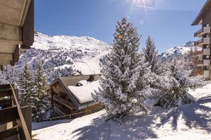 Un chalet de madera con techo inclinado, rodeado de árboles cubiertos de nieve y una montaña al fondo.