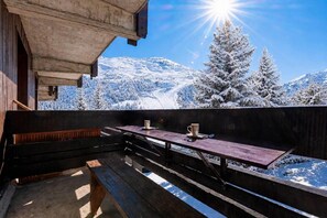 A wooden deck with a table and benches overlooking a snowy mountain landscape. - 350m from shops, floor -2, balcony, tv, 36m², Méribel-Mottaret (Les Allues)