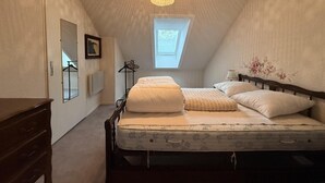 Une chambre avec un plafond en pente, un puits de lumière, un lit avec une literie blanche, une commode en bois et un luminaire suspendu.