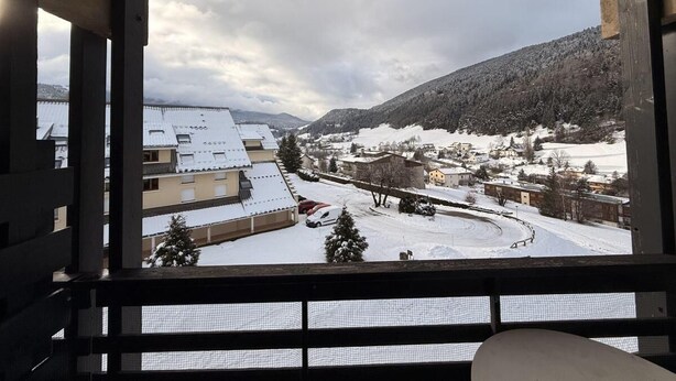 Une vue depuis une fenêtre donnant sur une ville enneigée, avec des bâtiments et une montagne en arrière-plan.