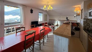Une cuisine spacieuse avec un grand îlot central, un coin repas avec une table rouge et une vue sur un paysage enneigé par les fenêtres.