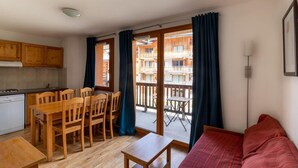A compact living space with a kitchenette, dining area, and a balcony with a view of a building.