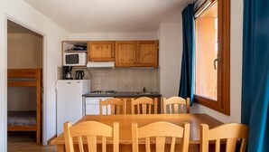A compact kitchen with wooden cabinets, a microwave, a stove, and a sink. There is a dining table with chairs and a bunk bed in the adjacent room.