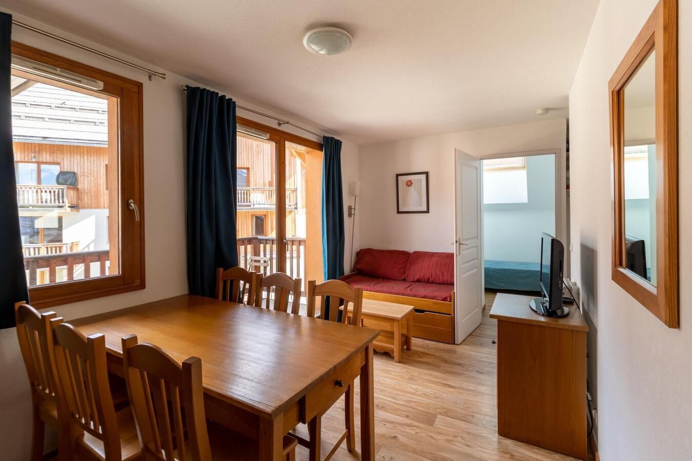 A cozy room with a wooden dining table, chairs, a red sofa, and a TV.