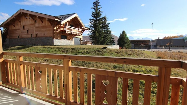 A wooden chalet with a balcony, set against a mountainous backdrop.