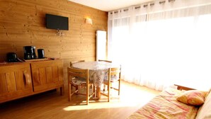 A cozy room with a wooden interior, a dining table with chairs, a sofa, a flat-screen TV mounted on the wall, and a window with curtains.