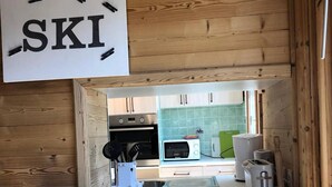 A kitchen with wooden walls, a white countertop, and various appliances including a microwave, toaster, and oven. - 50m from ski slopes, 2nd floor, balcony, tv, 66m², Alpe d'Huez (L'Alpe d'Huez)