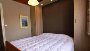 A bedroom with a single bed, a wooden headboard, a wall-mounted lamp, and a door with a curtain. - 50m from ski slopes, 2nd floor, balcony, tv, 66m², Alpe d'Huez (L'Alpe d'Huez)