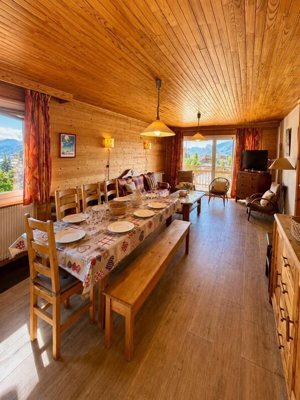 A wooden dining room with a table set for four, wooden chairs, and a bench.