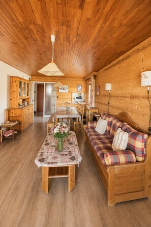 A cozy wooden interior with a dining area, sofa, and a table with a floral centerpiece.
