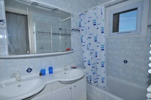 Bathroom features a double sink, shower area with glass door, and a small window above the shower.