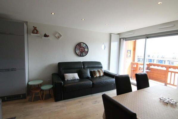 A modern living room with a black leather sofa, a dining table, and a small round table.