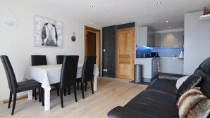 En moderne stue med en sort lædersofa, et spiseområde med bord og stole, og et køkken i baggrunden.