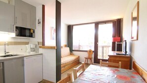 A compact hotel room with a kitchenette, a bed with a floral bedspread, a small desk, and a window with a view.