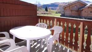 A wooden deck with a white table and chairs, overlooking a mountainous landscape.