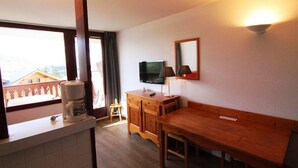Quarto com escrivaninha de madeira, televisão na parede, máquina de café no balcão e vista para o exterior pela janela.