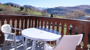 Uma varanda com uma mesa e duas cadeiras, dando vista para uma paisagem montanhosa.