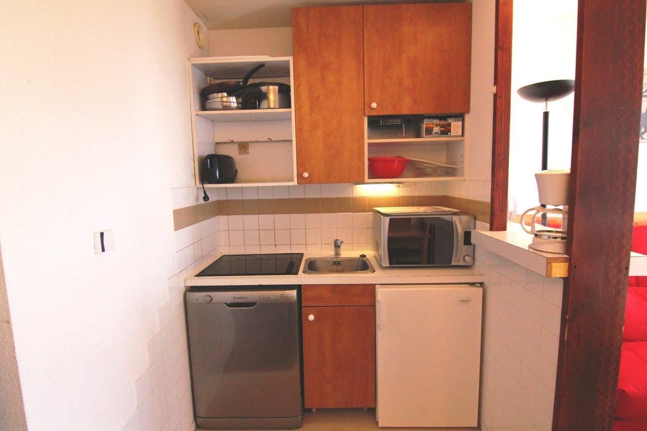 Cocina compacta con armarios de madera, microondas, lavavajillas y un refrigerador pequeño.