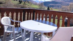 Un balcon avec une table et deux chaises, donnant sur un paysage montagneux.