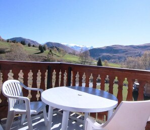 Un balcón con mesa y dos sillas, con vistas a un paisaje montañoso.