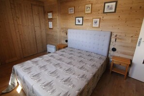 Ein Zimmer mit Holzwand, einem Bett, zwei Nachttischen und gerahmten Bildern an der Wand.