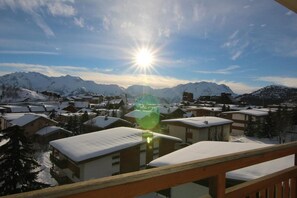 Ein verschneites Dorf mit einer markanten Bergkette im Hintergrund und einer hellen Sonne.