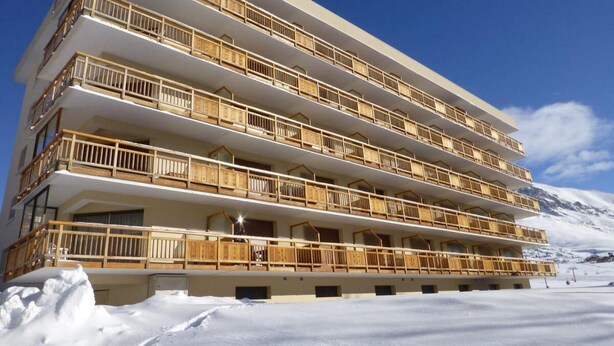 Et hotel med flere etager og balkoner, med sneklædte bjerge i baggrunden.