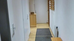 En smal gang med trægulv, en træbænk, et lille bord og en vægmonteret hylde med en skål.