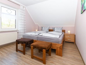 A bedroom with a sloped ceiling, a bed with grey bedding, two bedside tables, and a window with curtains.