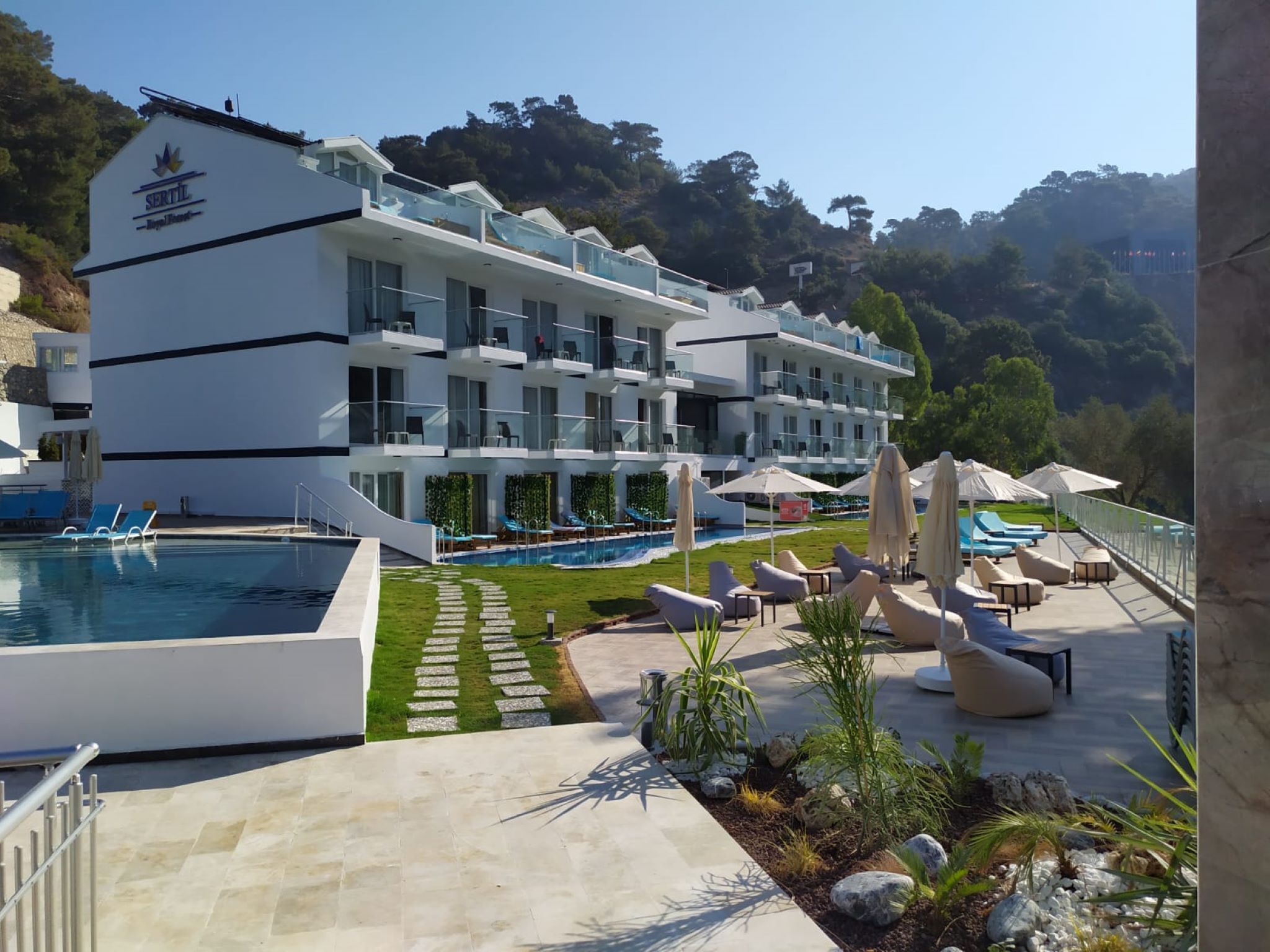 Um hotel moderno com piscina, área de estar externa e vista para as colinas ao redor.