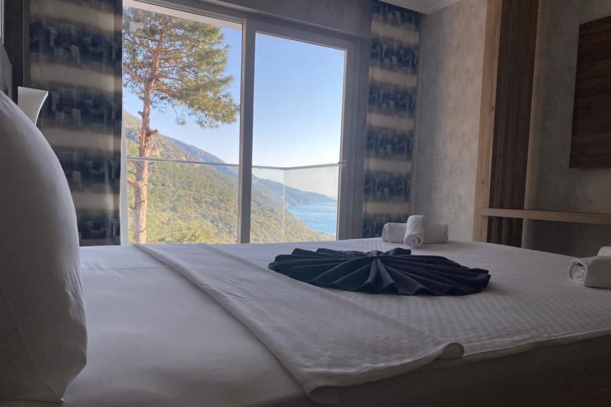 Une chambre d’hôtel avec un lit, une fenêtre donnant sur la montagne et un rideau orné d’un motif bleu.