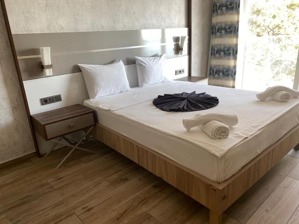Une chambre d’hôtel moderne avec un grand lit, une tête de lit en bois et une table de chevet avec une lampe.