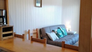Une pièce chaleureuse avec une table et des bancs en bois, un lit avec des oreillers et un tableau encadré au mur.