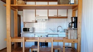 Une cuisine avec des meubles blancs, un four à micro-ondes, une machine à café et des chaises en bois.