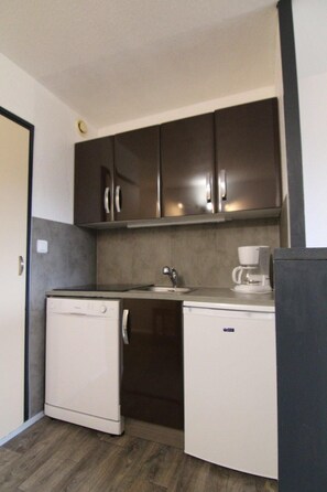 A compact kitchenette with dark cabinets, a small sink, and a coffee maker.