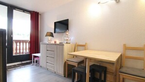 A small room with a wooden table and chairs, a TV mounted on the wall, and a sliding glass door leading to an outdoor balcony. - 100m from ski slopes, 3rd floor, balcony, tv, ski locker, 24m², Alpe d'Huez (L'Alpe d'Huez)