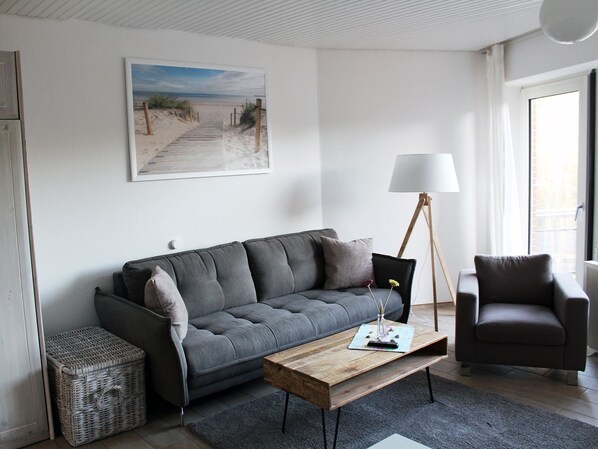 A modern living room with a grey sofa, a wooden coffee table, a floor lamp, and a framed beach painting on the wall.