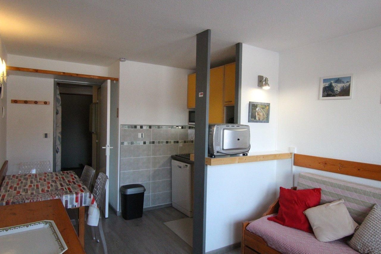 A compact room with a dining table, a sofa, a small kitchen area, and a mirror.