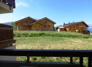 Edifici de tipus xalet de fusta amb un balcó, envoltat d'una zona verda i muntanyes al fons.