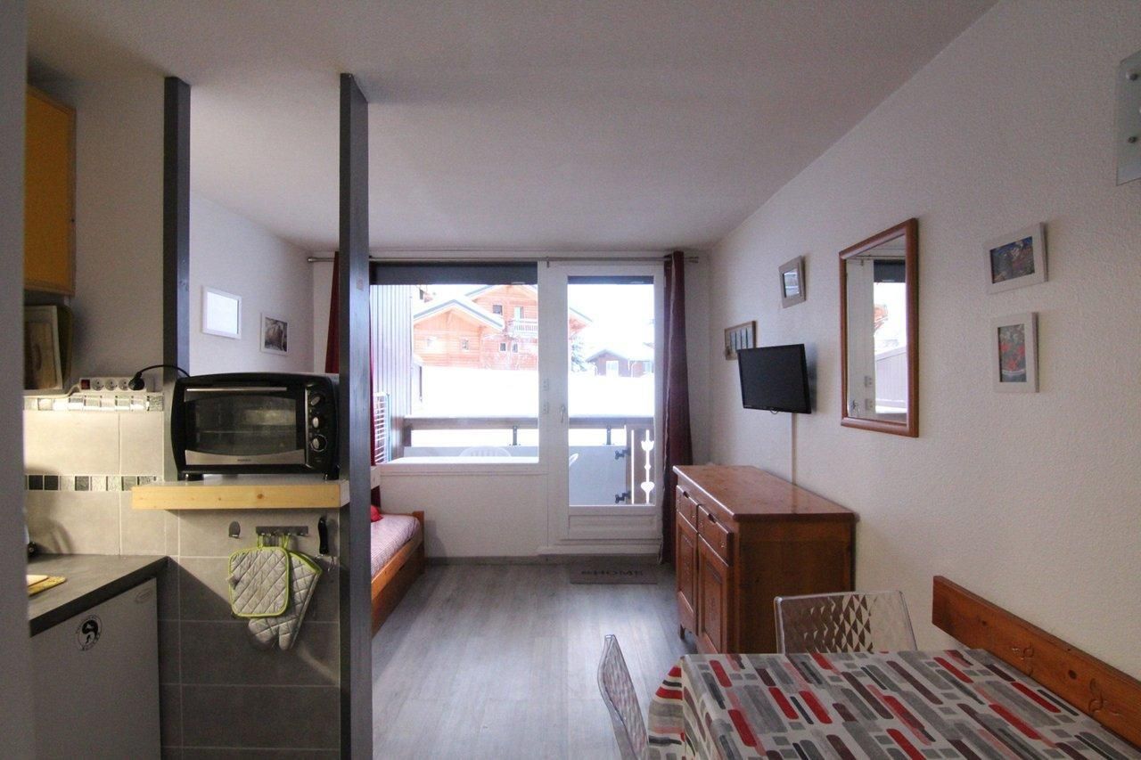 A compact living space with a kitchenette, a bed, a TV, and a window with a view of buildings outside.
