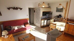 Een woonkamer met een rode bank, een houten salontafel en een televisie. Achtergrond zichtbaar van een keuken met een eethoek.