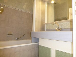 Bathroom features a bathtub and sink with a handrail and mirror.