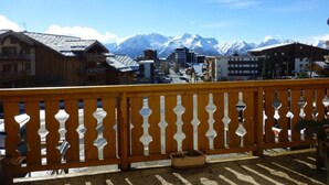 Een houten balkon met uitzicht op besneeuwde bergen en een stad eronder.