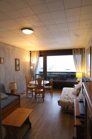 A room with a bed, a sofa, a table, and a window with curtains.
